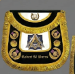 Black and gold embroidered Masonic apron on a gray background.