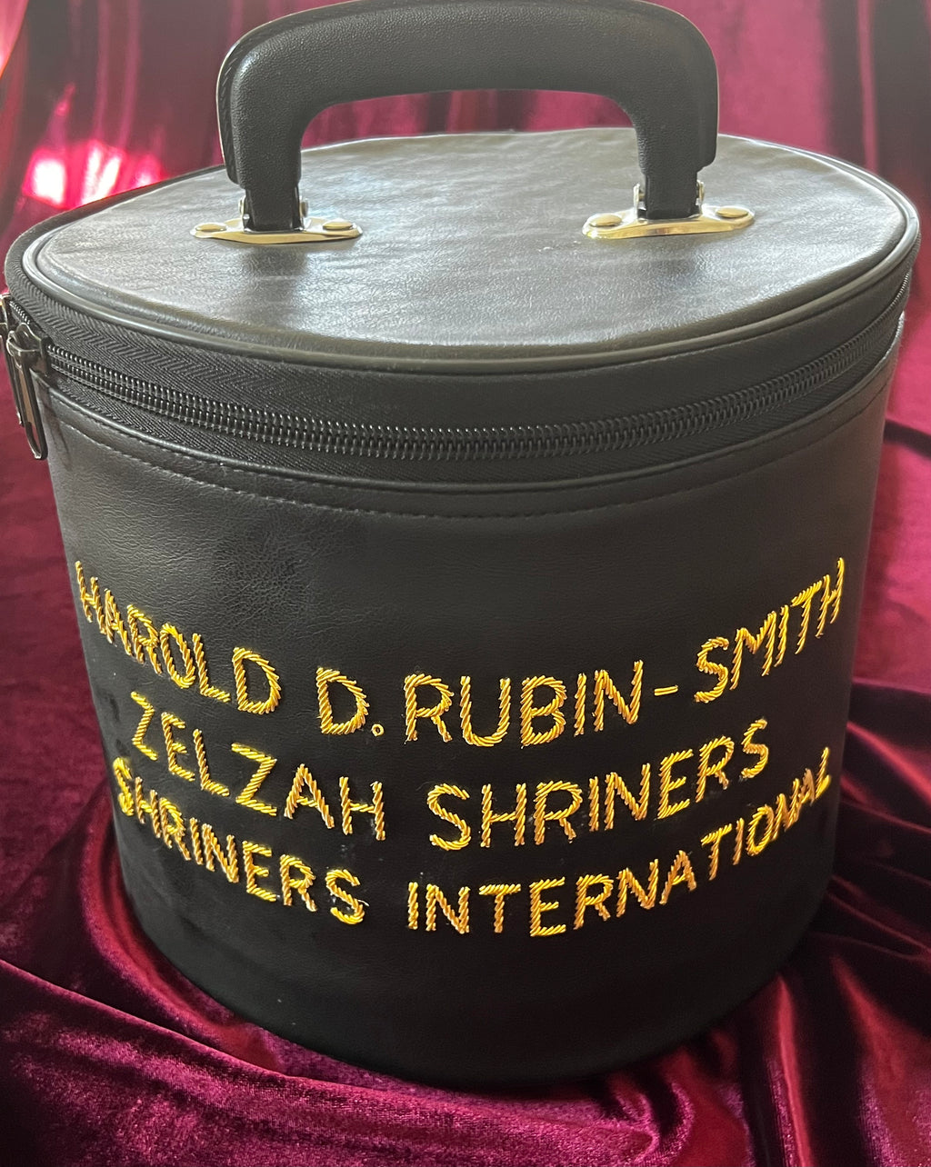Black Zelzah Shriners carry case with gold name embroidery and top handle, shown alone on burgundy fabric