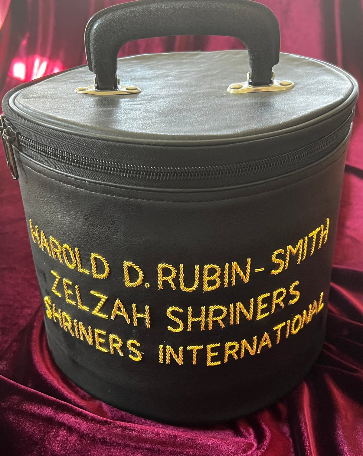 Black Zelzah Shriners carry case with gold name embroidery and top handle, shown alone on burgundy fabric