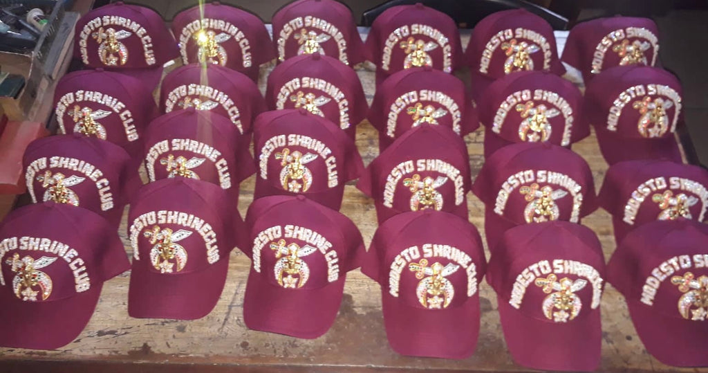 Group of burgundy Shriners club caps with jeweled club lettering and Shrine emblems; example designs