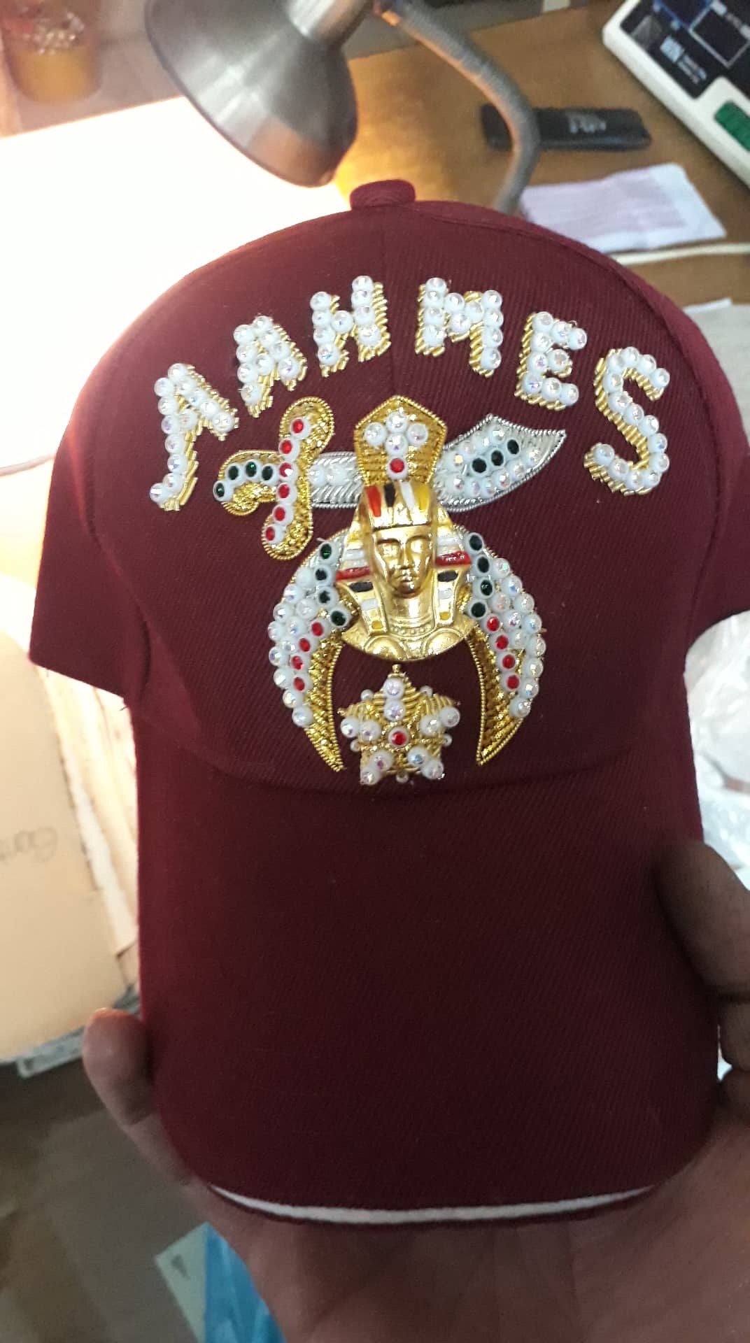 Burgundy jeweled Shriner cap with jeweled emblem and lettering, photographed in hand
